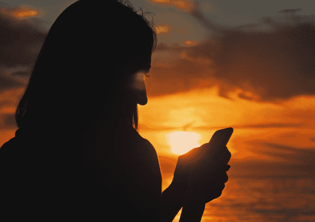 Person using cell phone at sunset